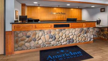 A reception desk with a stone facade, wooden paneling, and a logo for AmericInn by Wyndham.