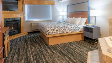 A bedroom with a bed, a TV, a fireplace, a nightstand, and a bathroom.