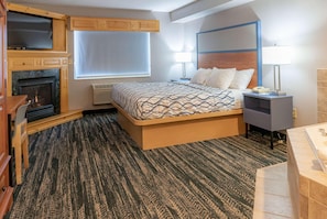 A bedroom with a bed, a TV, a fireplace, a nightstand, and a bathroom. - Americinn By Wyndham Wabasha (Wabasha)