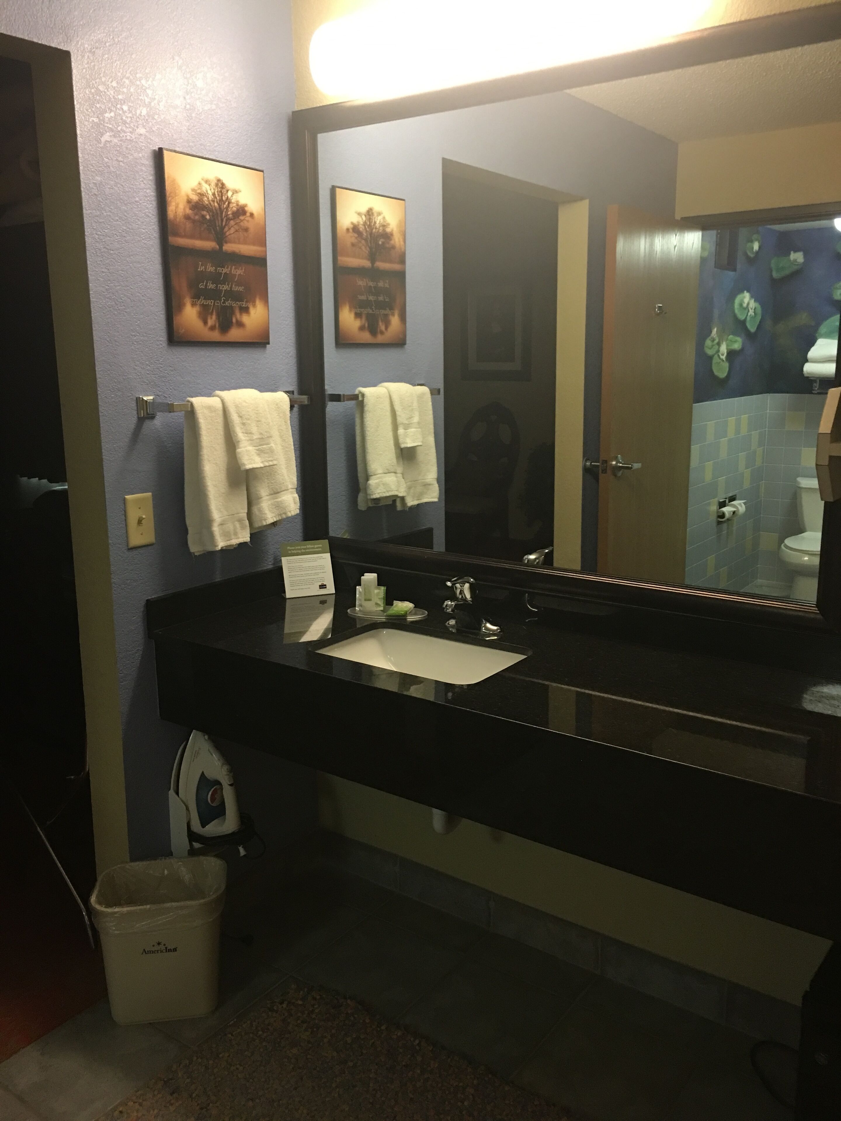 A bathroom with a black sink, two white towels, a mirror, and a trash bin.