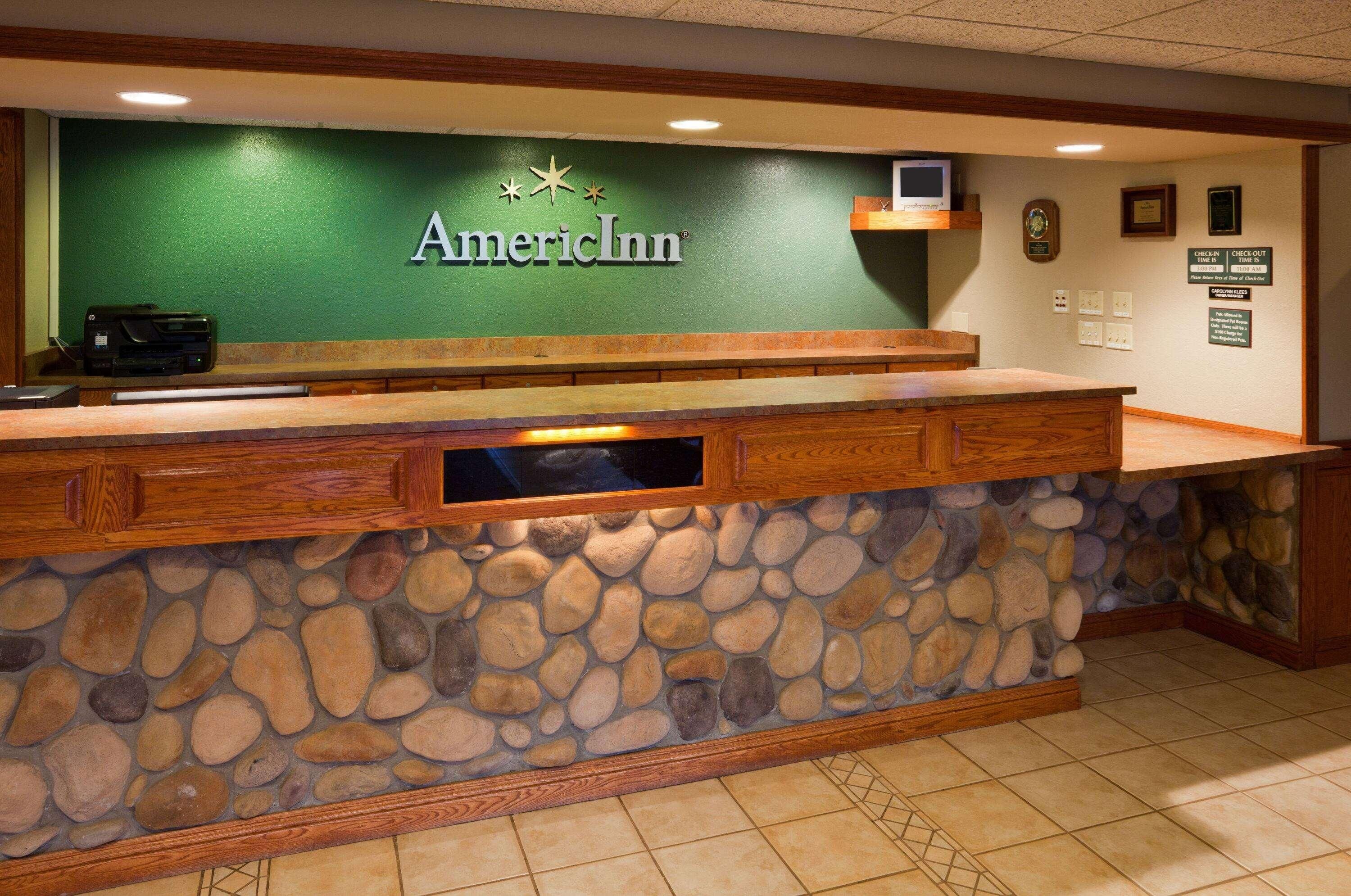 A reception desk with a stone facade, a wooden counter, and the AmericInn logo.