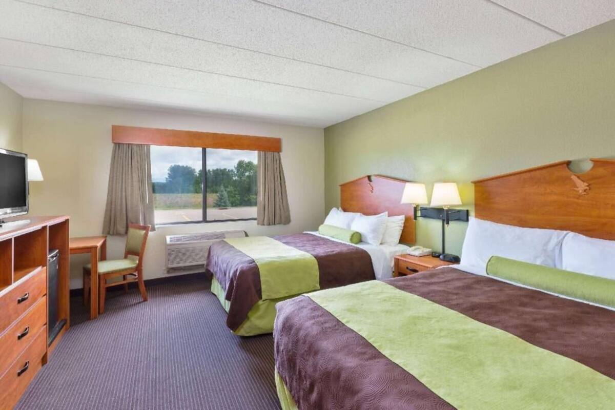 A hotel room with two beds, a desk, a TV, and a window with curtains.