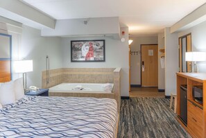 Quarto de hotel com uma cama grande, banheira, escrivaninha com abajur e espelho.