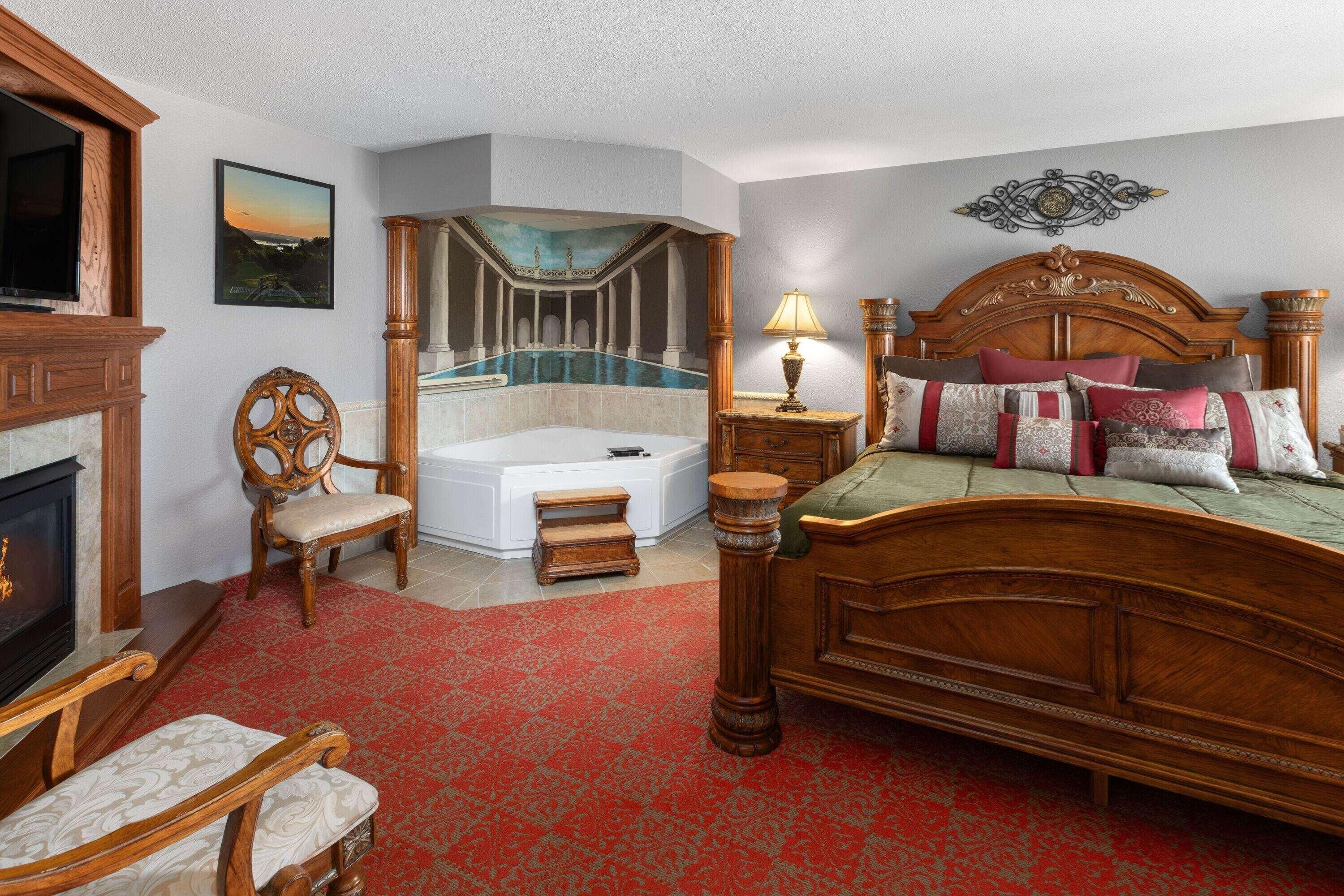 A bedroom with a large bed, a fireplace, a bathtub, and a view of a pool.
