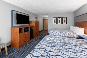 Habitación de hotel con televisión, armario de madera, dos camas con ropa de cama estampada, un escritorio pequeño y cuadros en la pared.