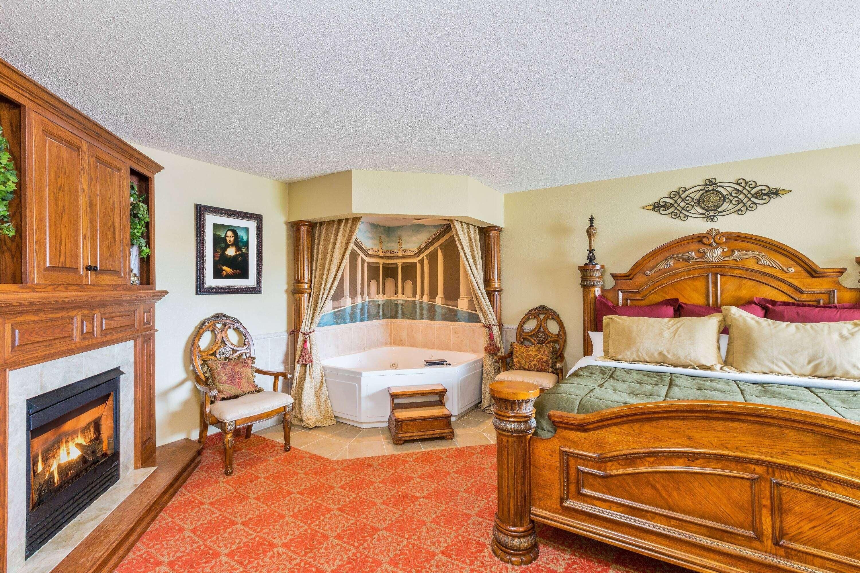 A bedroom with a large bed, a fireplace, a bathtub, and a wooden cabinet.