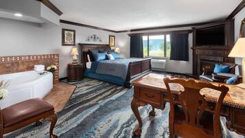 A hotel room with a large bed, a sitting area with a sofa and armchair, a dining table, and a fireplace.