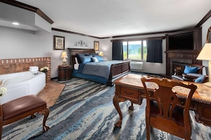 Una habitación de hotel con una cama grande, una sala de estar con sofá y sillón, una mesa de comedor y una chimenea.