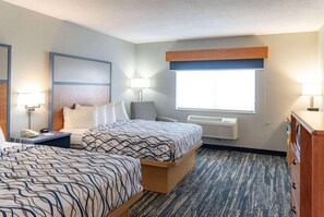 Une chambre d’hôtel avec deux lits, un bureau avec un téléphone, une lampe, une fenêtre et un appareil de climatisation.
