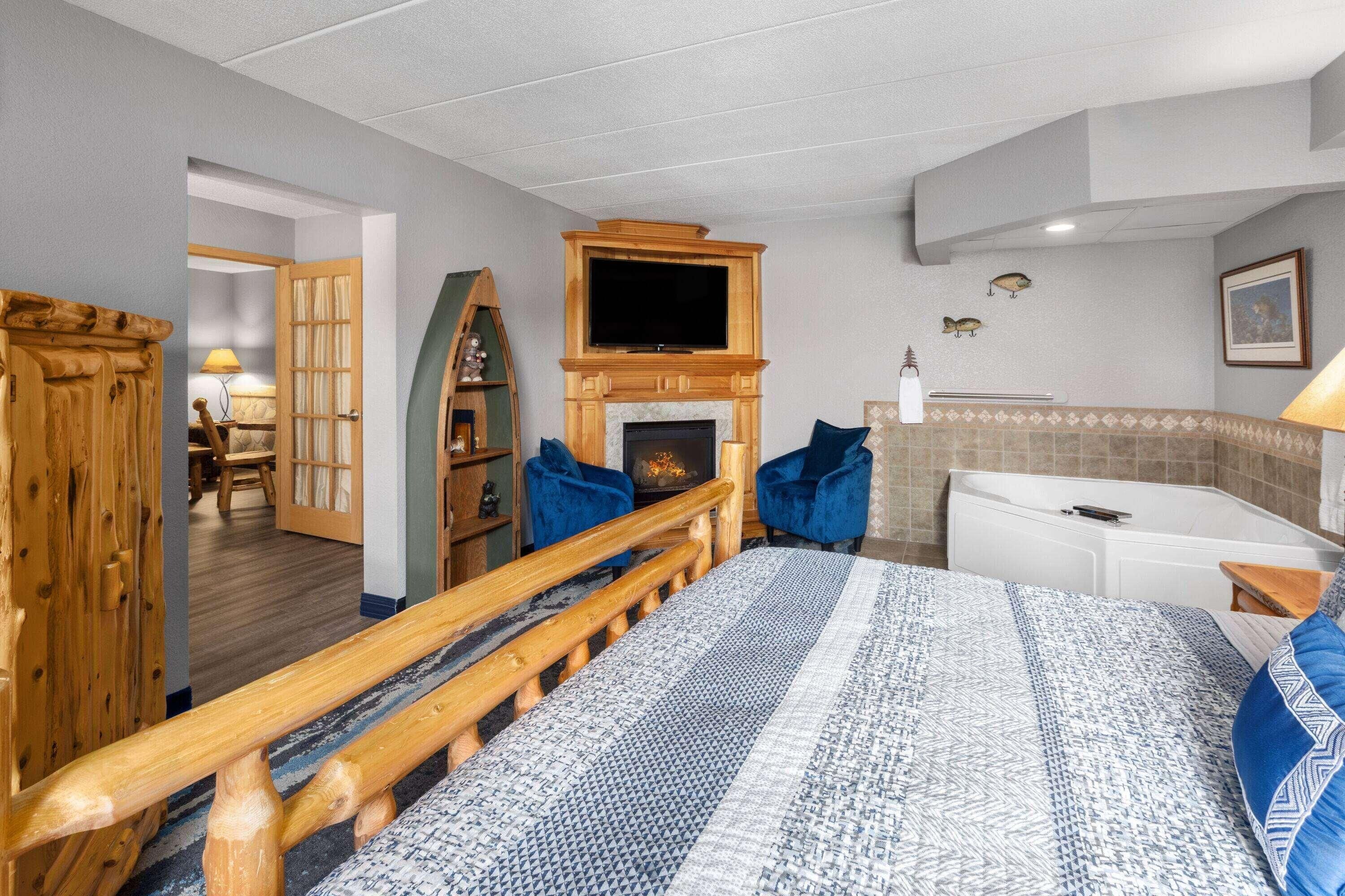 Un dormitorio con cama, televisor sobre la chimenea, escritorio y baño al fondo.