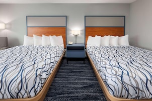 Habitación de hotel con dos camas, una mesita de noche con lámpara y suelo alfombrado.