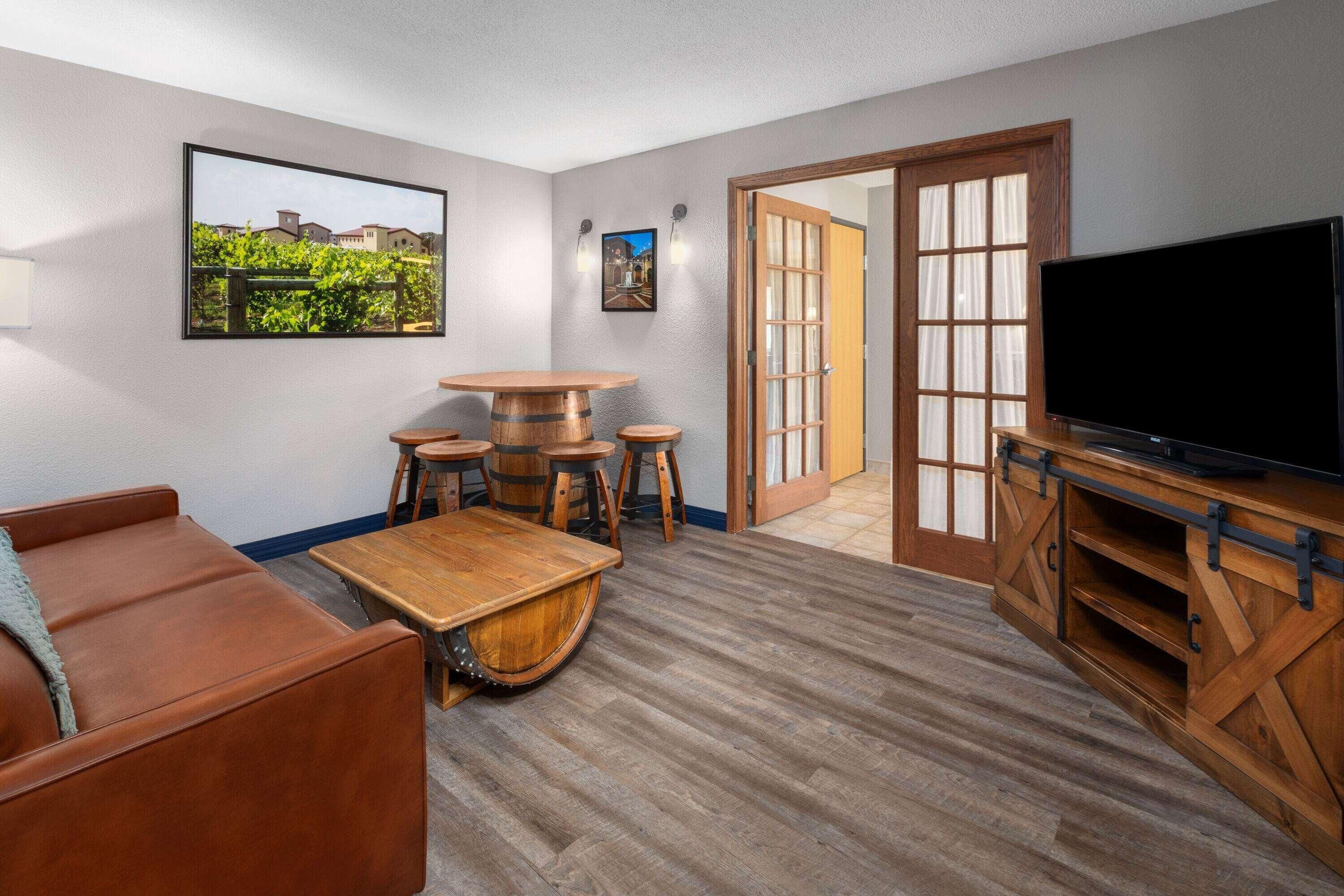 A living room with a wooden coffee table, a leather sofa, a TV, and a door leading outside.