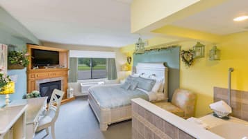 Un dormitorio con cama, televisor, chimenea, baño con bañera y vistas al exterior.