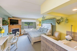 Un dormitorio con cama, televisor, chimenea, baño con bañera y vistas al exterior.