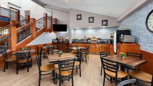 A restaurant with wooden tables and chairs, a kitchen area, and a staircase. - Americinn By Wyndham Wabasha (Wabasha)