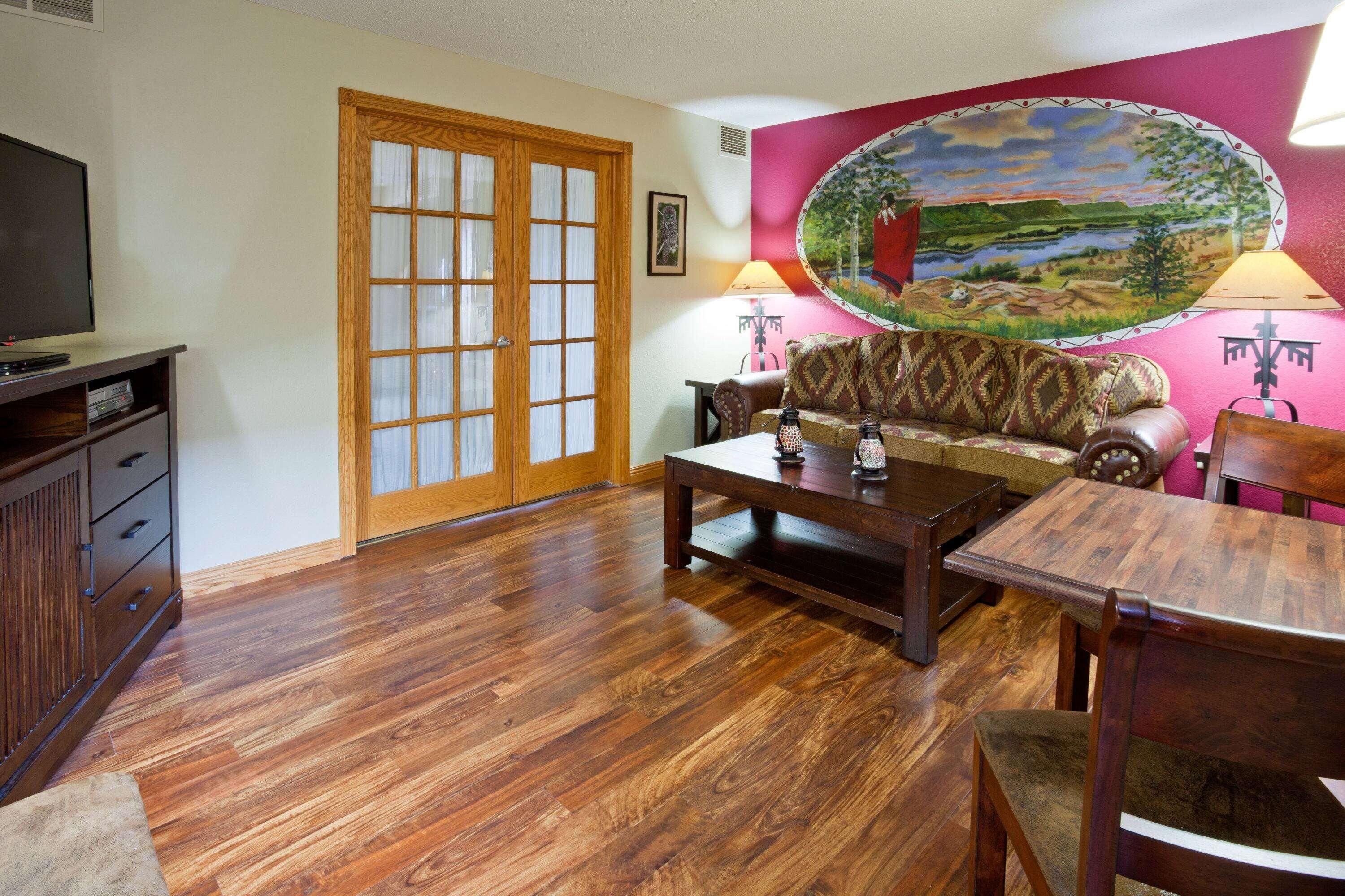 A living room with a wooden floor, a sofa, a coffee table, a TV, and a painting on the wall.