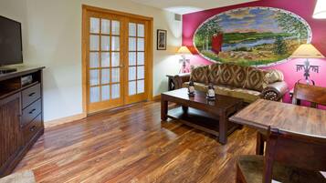 A living room with a wooden floor, a sofa, a coffee table, a TV, and a painting on the wall.