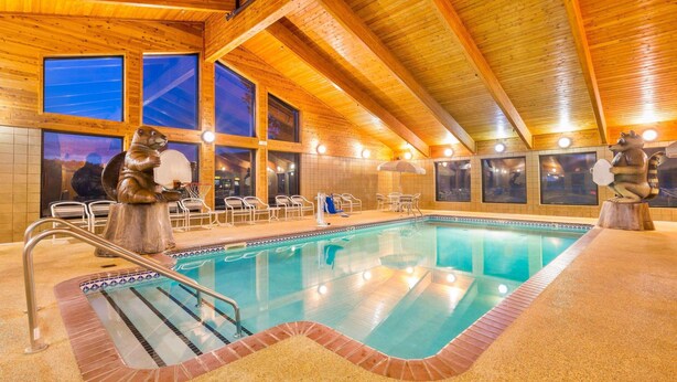 An indoor swimming pool with wooden beams, clear glass windows, and two animal sculptures. - Americinn By Wyndham Wabasha (Wabasha)