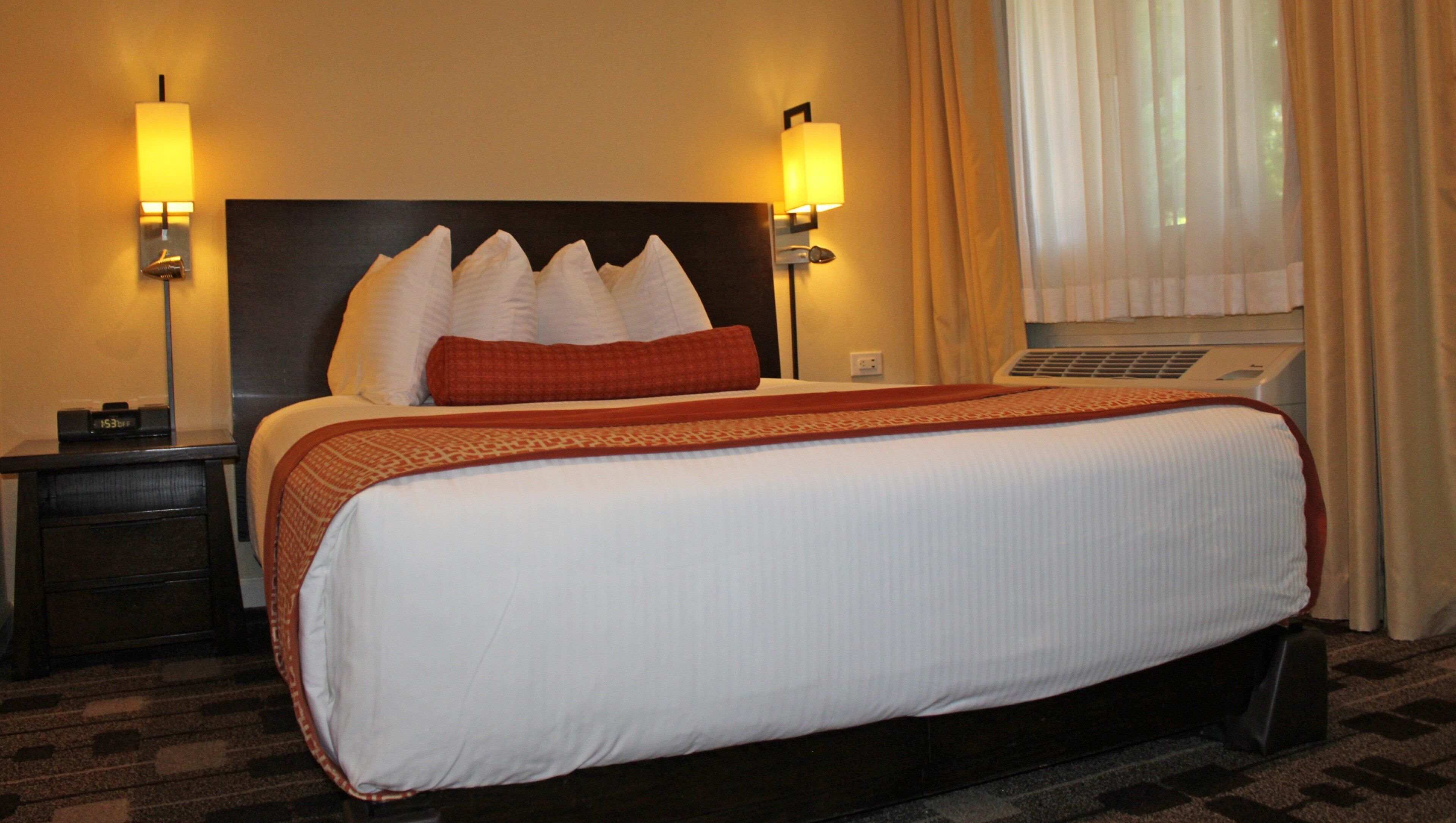 A hotel room with a large bed, two bedside lamps, a nightstand, and a window with curtains.