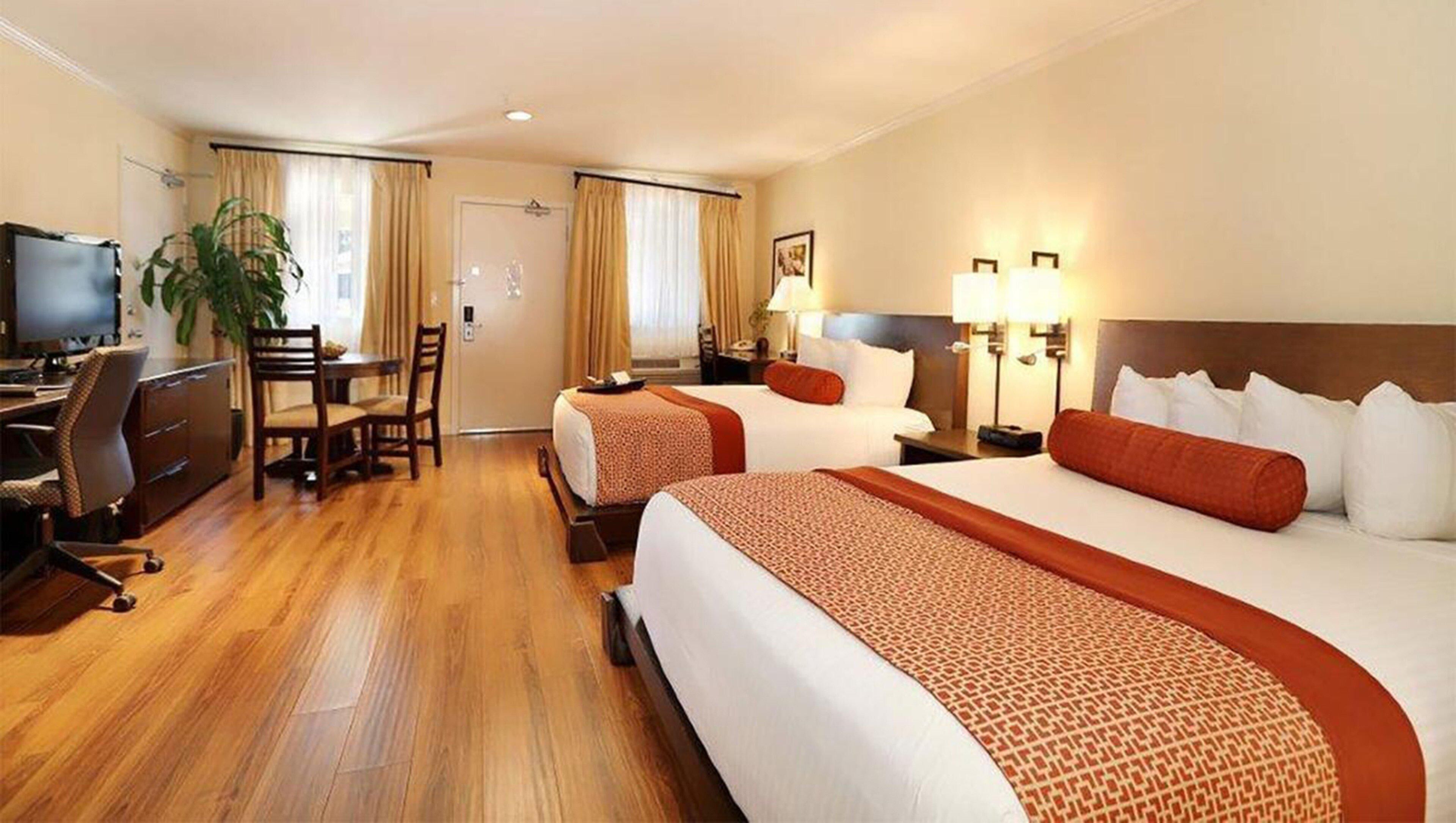 Une chambre d’hôtel avec deux lits, un bureau, une chaise, une télévision et une plante.