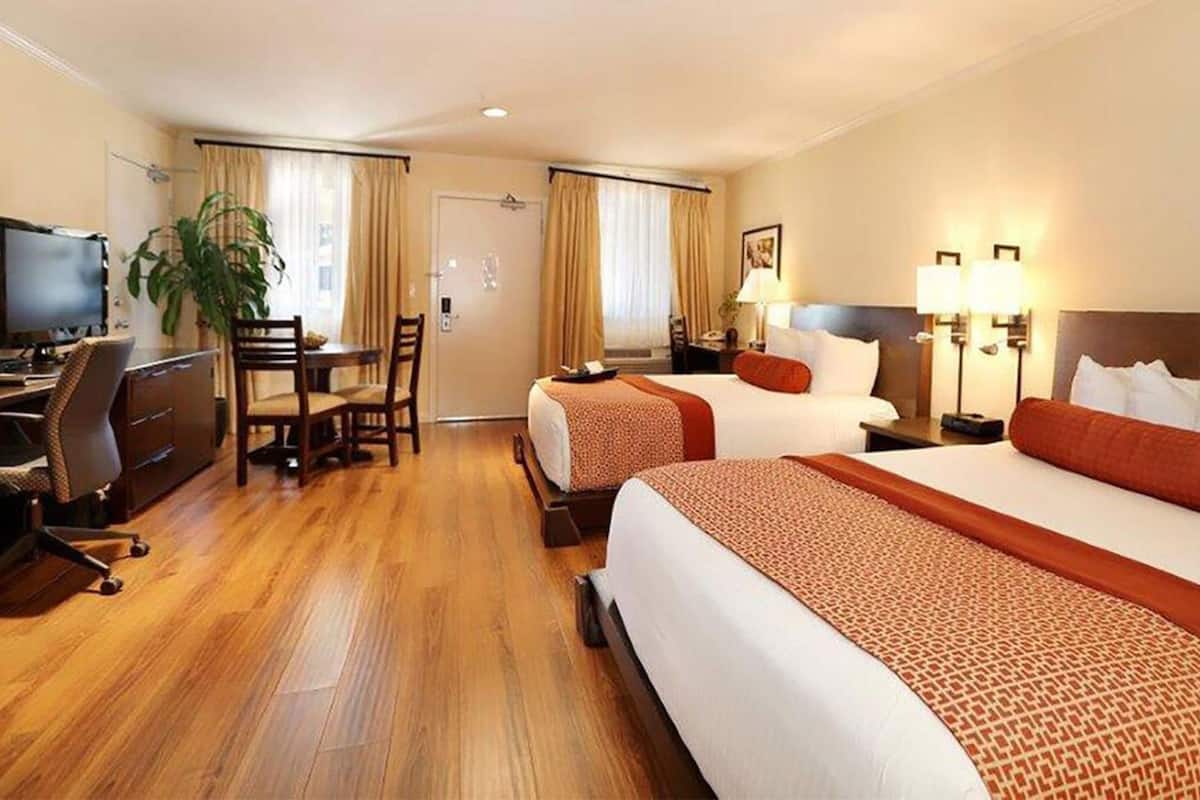 A hotel room with two beds, a desk, a chair, a television, and a plant.