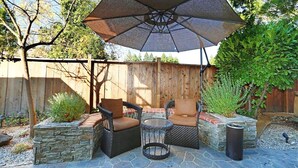 Een terras buiten met twee rieten stoelen, een ronde tafel en een grote parasol.
