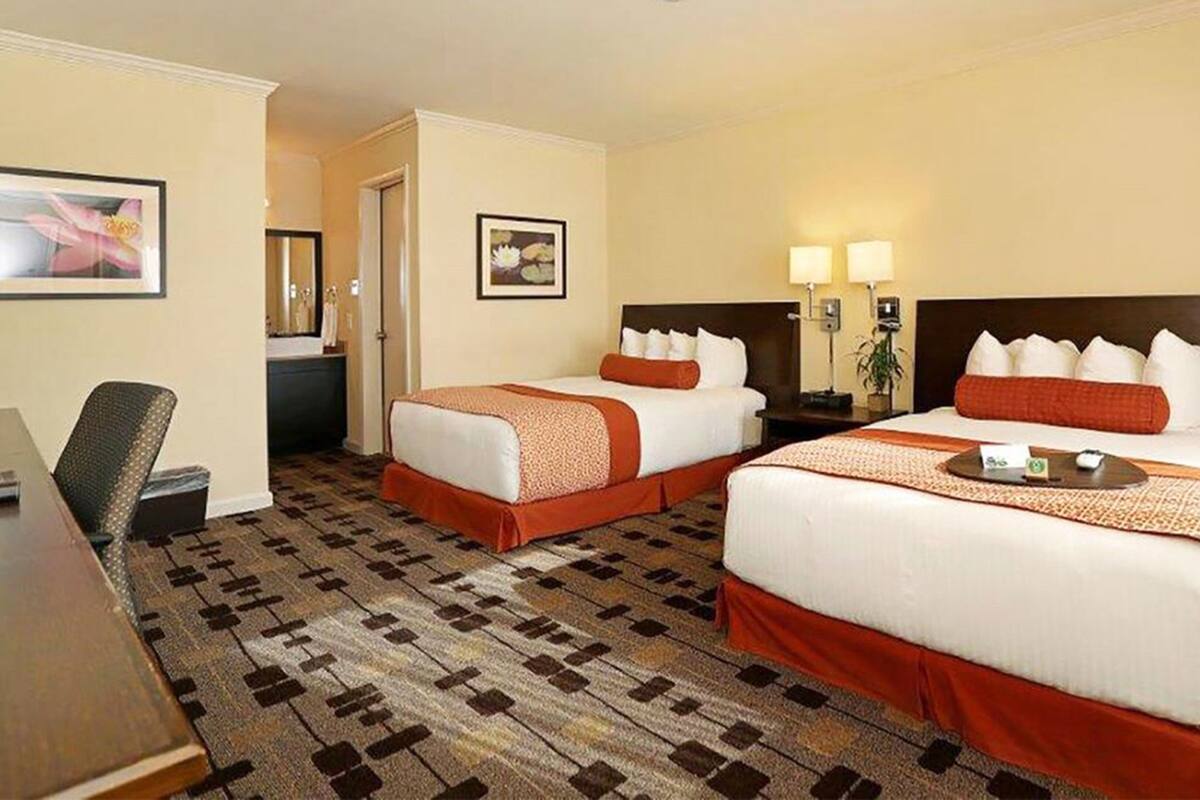 A hotel room with two beds, a desk, and a chair.