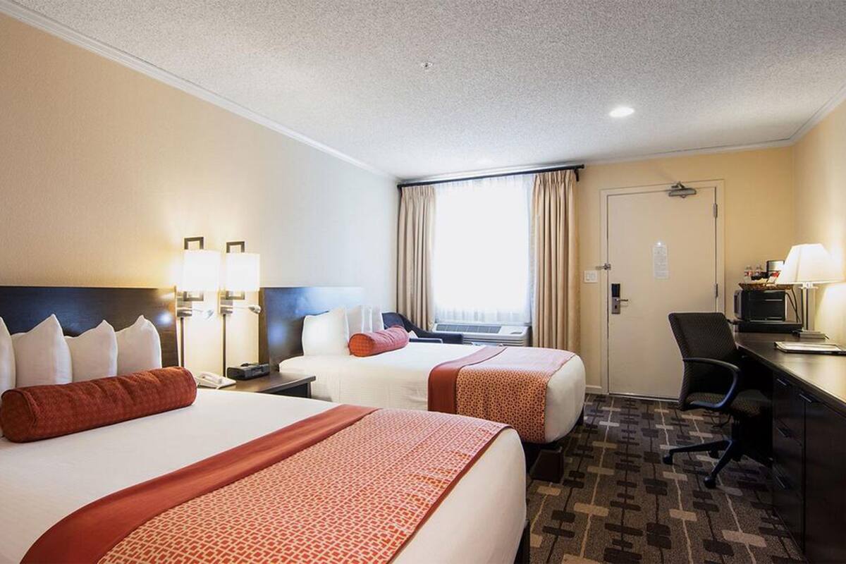 A hotel room with two beds, a desk, a chair, and a window with curtains.