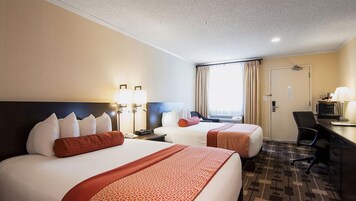 Habitación de hotel con dos camas, un escritorio, una silla y una ventana con cortinas.