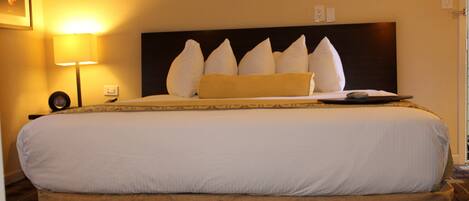 Una habitación de hotel con una cama grande, una mesita de noche con una lámpara y un reloj de pared.