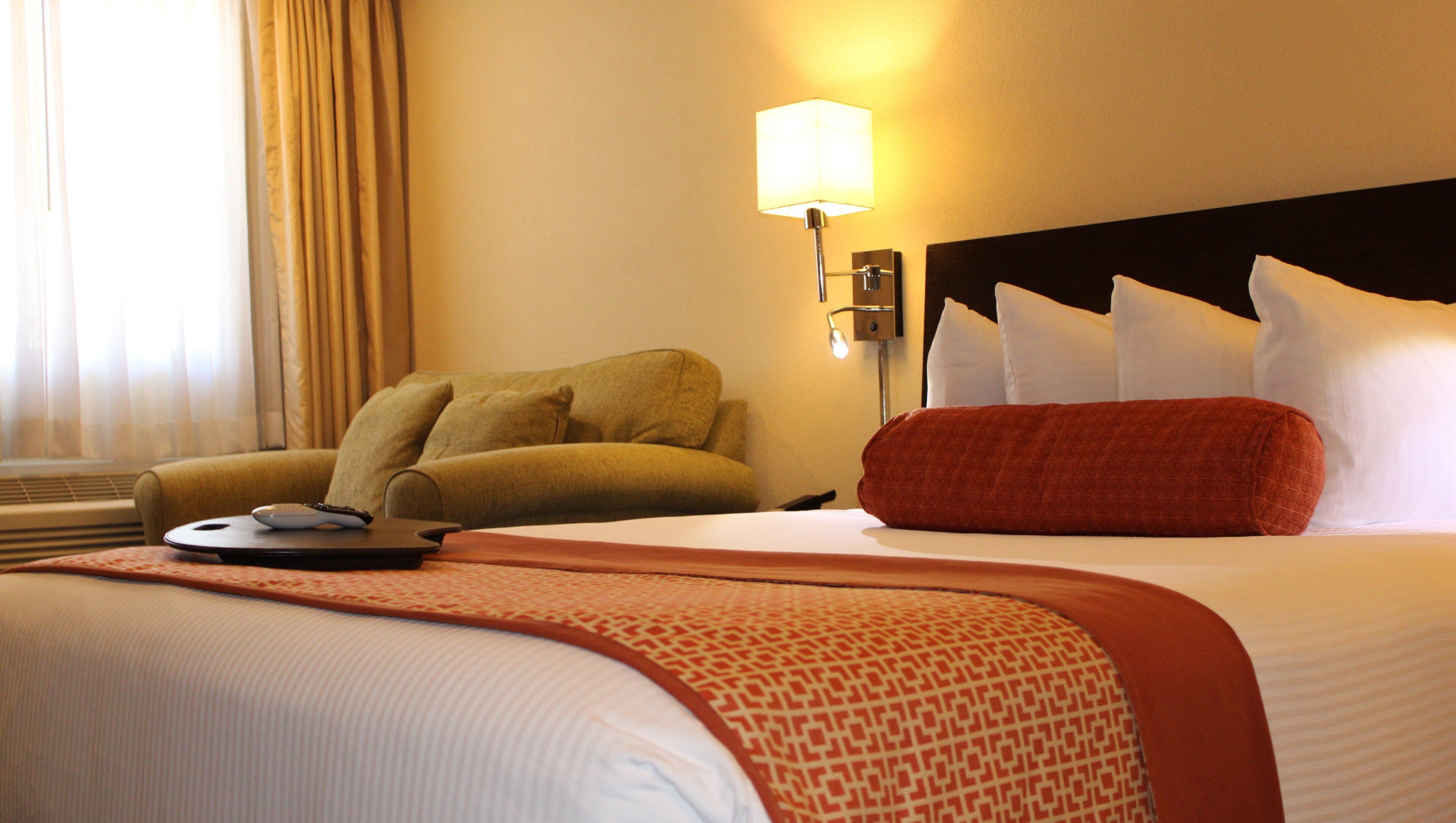 Een hotelkamer met een bed, een bank, een lamp en een afstandsbediening op de bank.