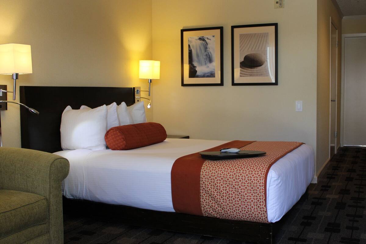 A hotel room with a bed, two wall-mounted lamps, a framed picture of a waterfall, and a framed picture of a hat.