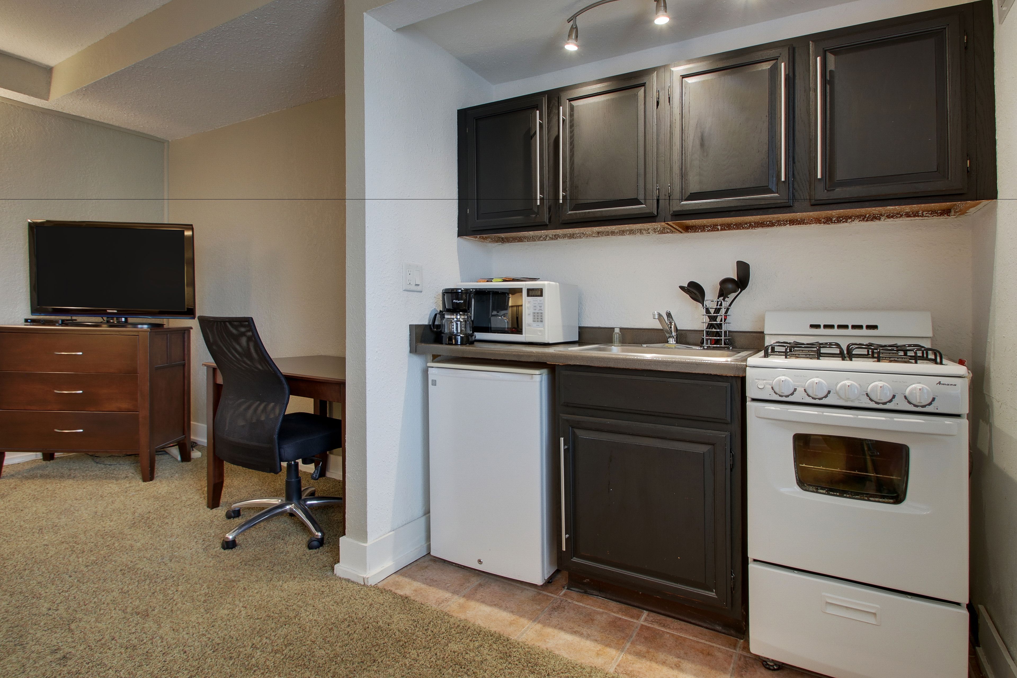 A compact kitchen with dark cabinets, a microwave, a gas stove, and a small refrigerator.