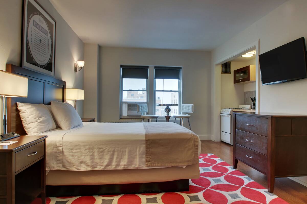 Ein Hotelzimmer mit Bett, Nachttischen, Schreibtisch, Stuhl, Fernseher und Fenster.