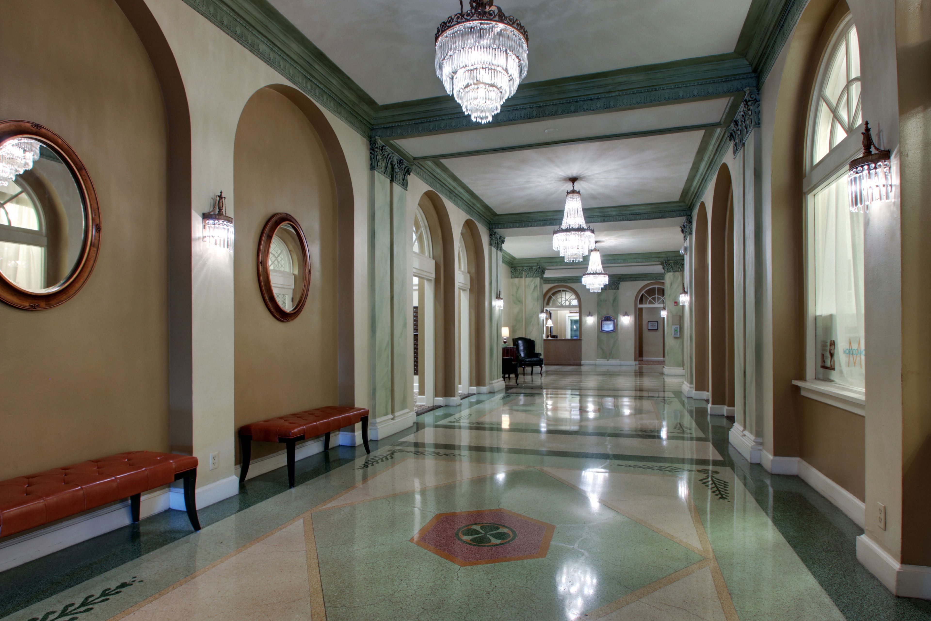 A spacious hallway with a polished floor, benches, and chandeliers.