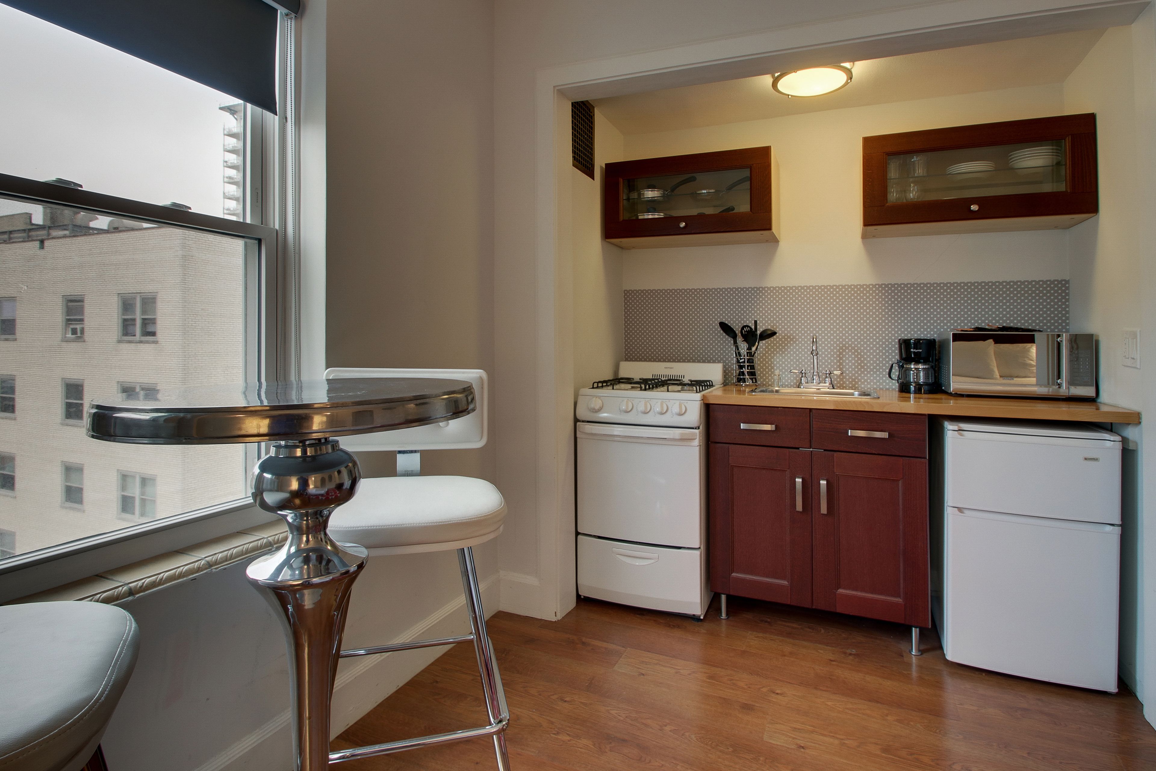 A compact kitchen with a stove, microwave, and refrigerator. There's a window with a view of buildings outside.