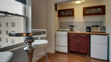 A compact kitchen with a stove, microwave, and refrigerator. There's a window with a view of buildings outside.
