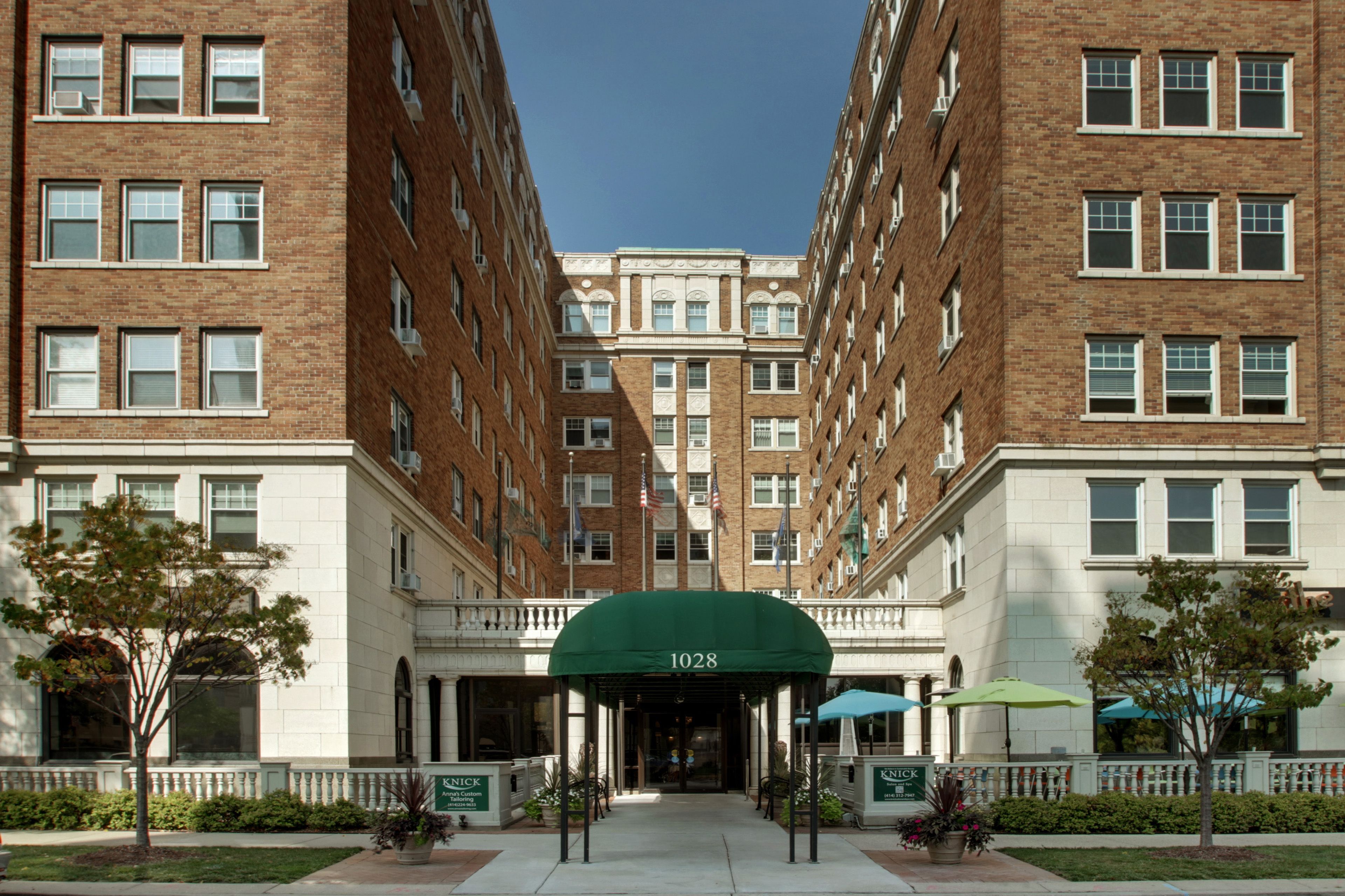 A multi-story hotel with a central entrance, brick facade, and a green awning with the number 1028.