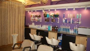 Un salón de belleza con varias sillas de peluquería, estantes con productos capilares y una lámpara de araña.