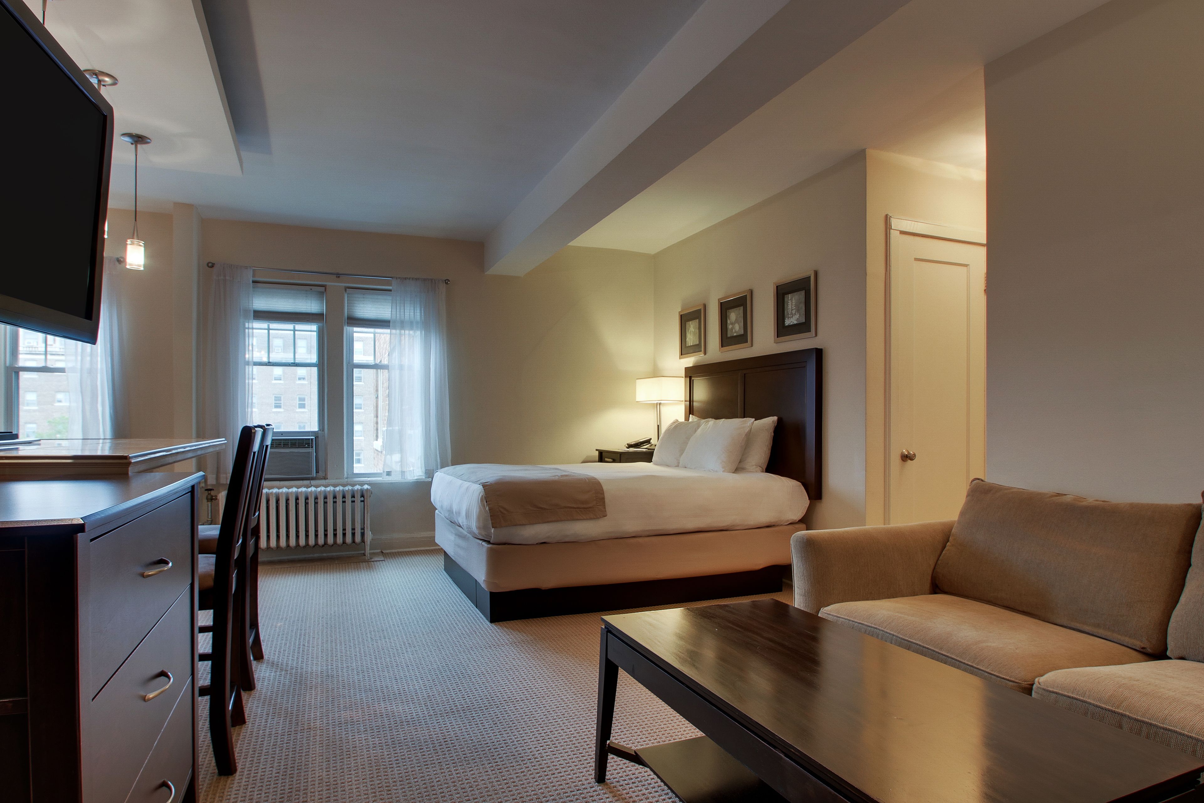 Ein Hotelzimmer mit einem Bett, einem Sofa, einem Schreibtisch mit Schubladen, einem Fernseher und einem Fenster mit Vorhängen.