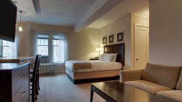 Ein Hotelzimmer mit einem Bett, einem Sofa, einem Schreibtisch mit Schubladen, einem Fernseher und einem Fenster mit Vorhängen.