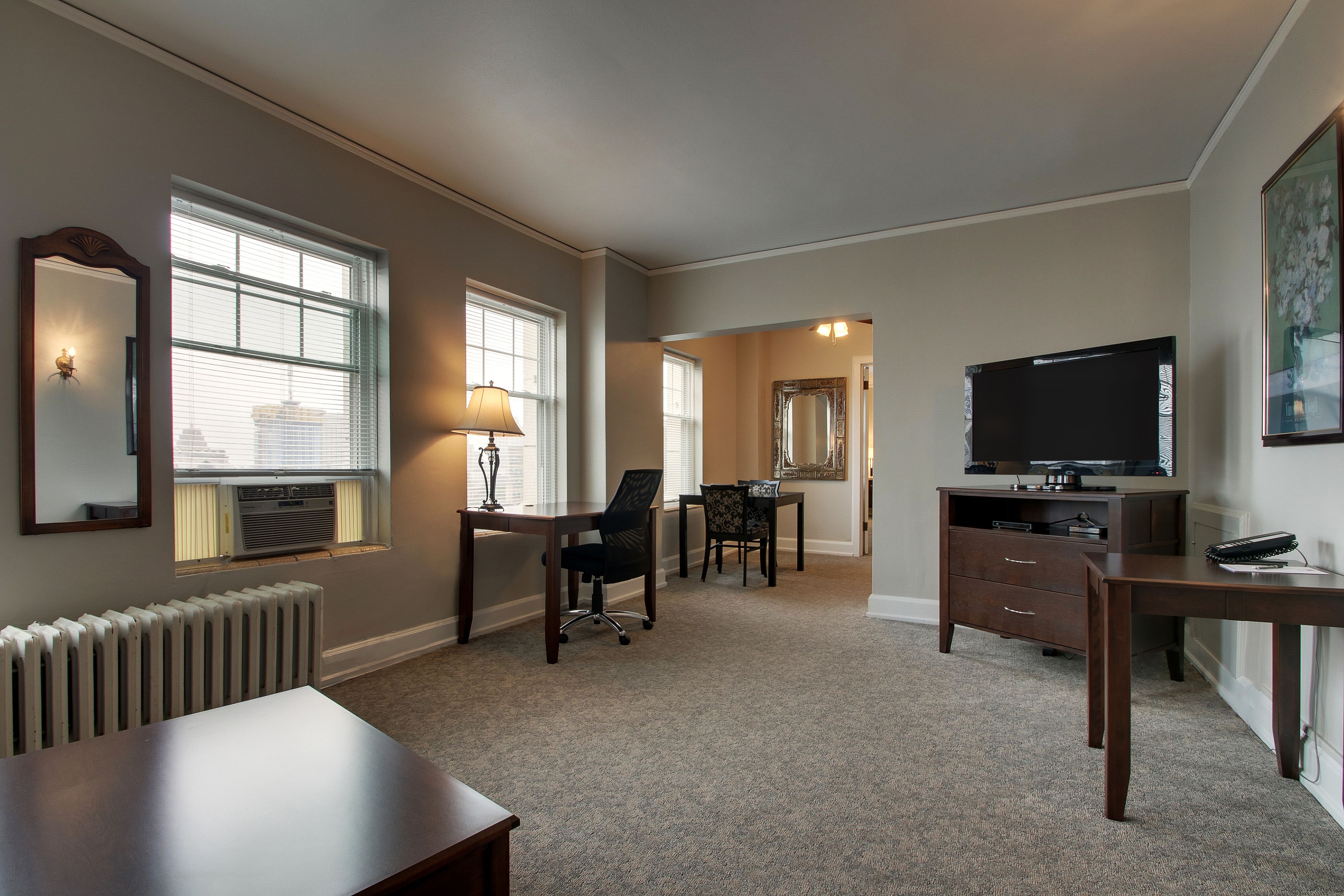 A room with a large window, a desk, a chair, a television, and a radiator.