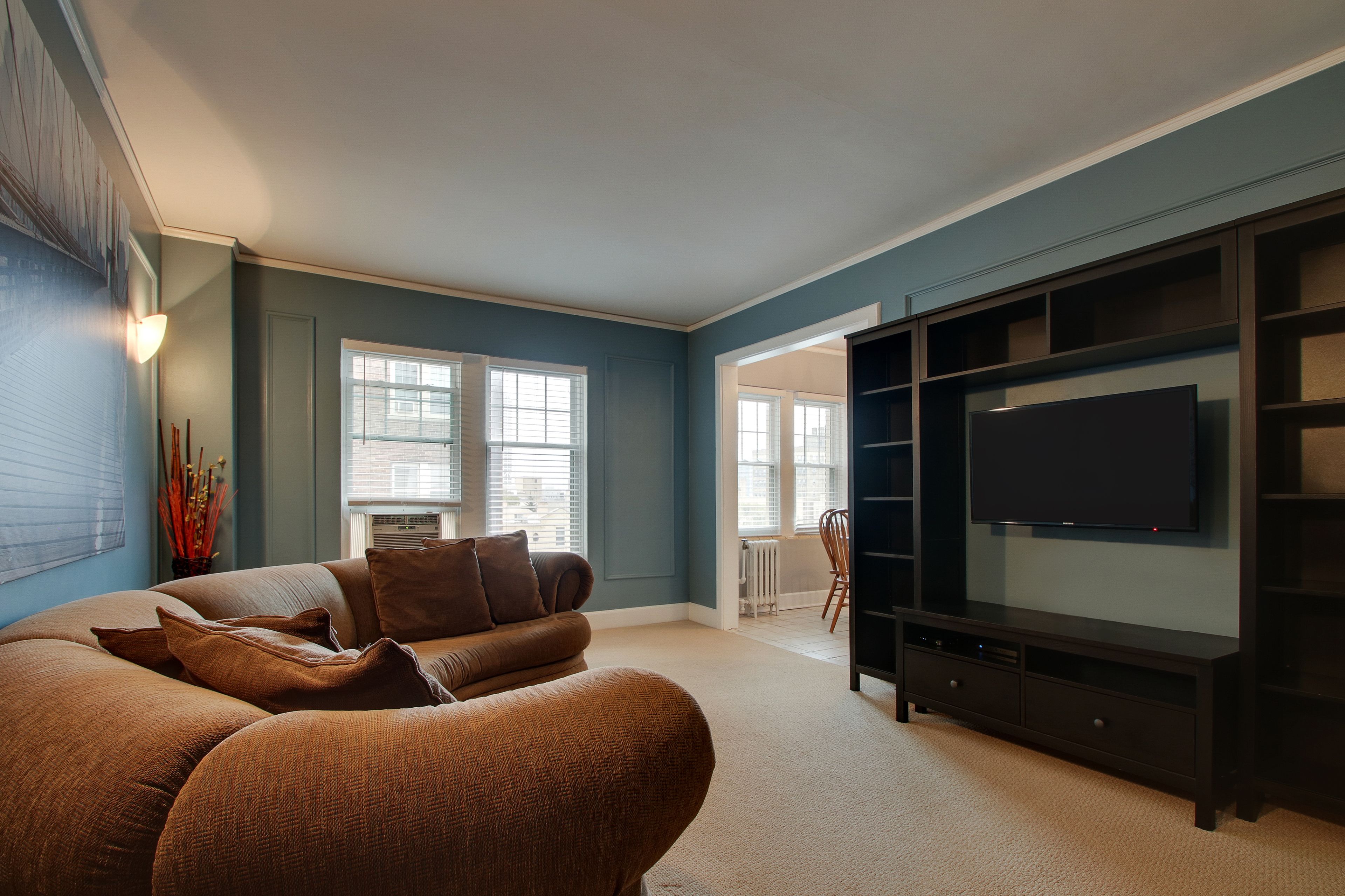Una sala de estar con un sofá modular, un televisor de pantalla plana sobre un mueble negro y un ventanal con persianas.