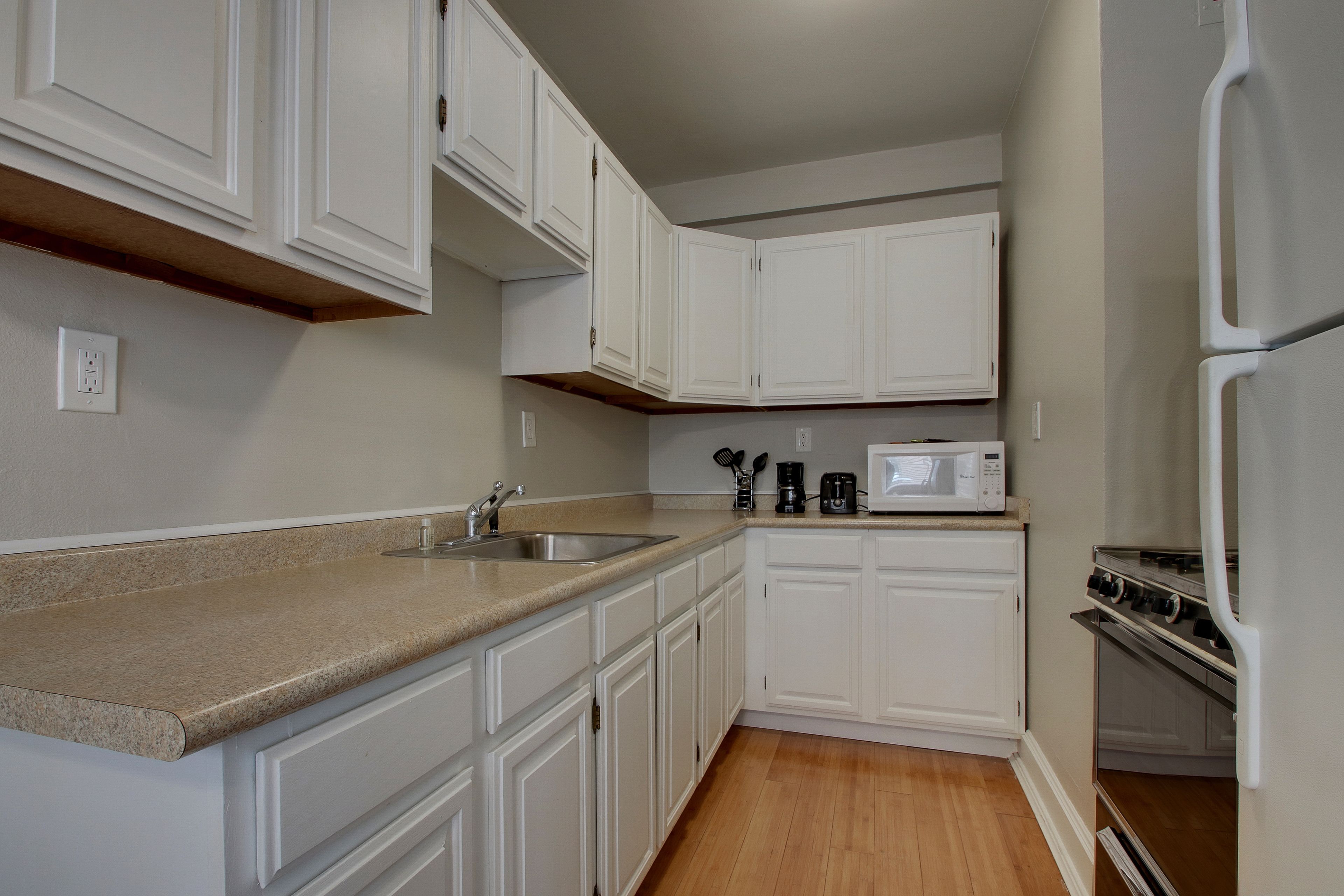 A kitchen with white cabinets, a granite countertop, a microwave, and a stove.