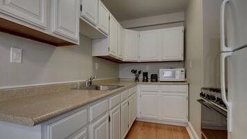 A kitchen with white cabinets, a granite countertop, a microwave, and a stove.