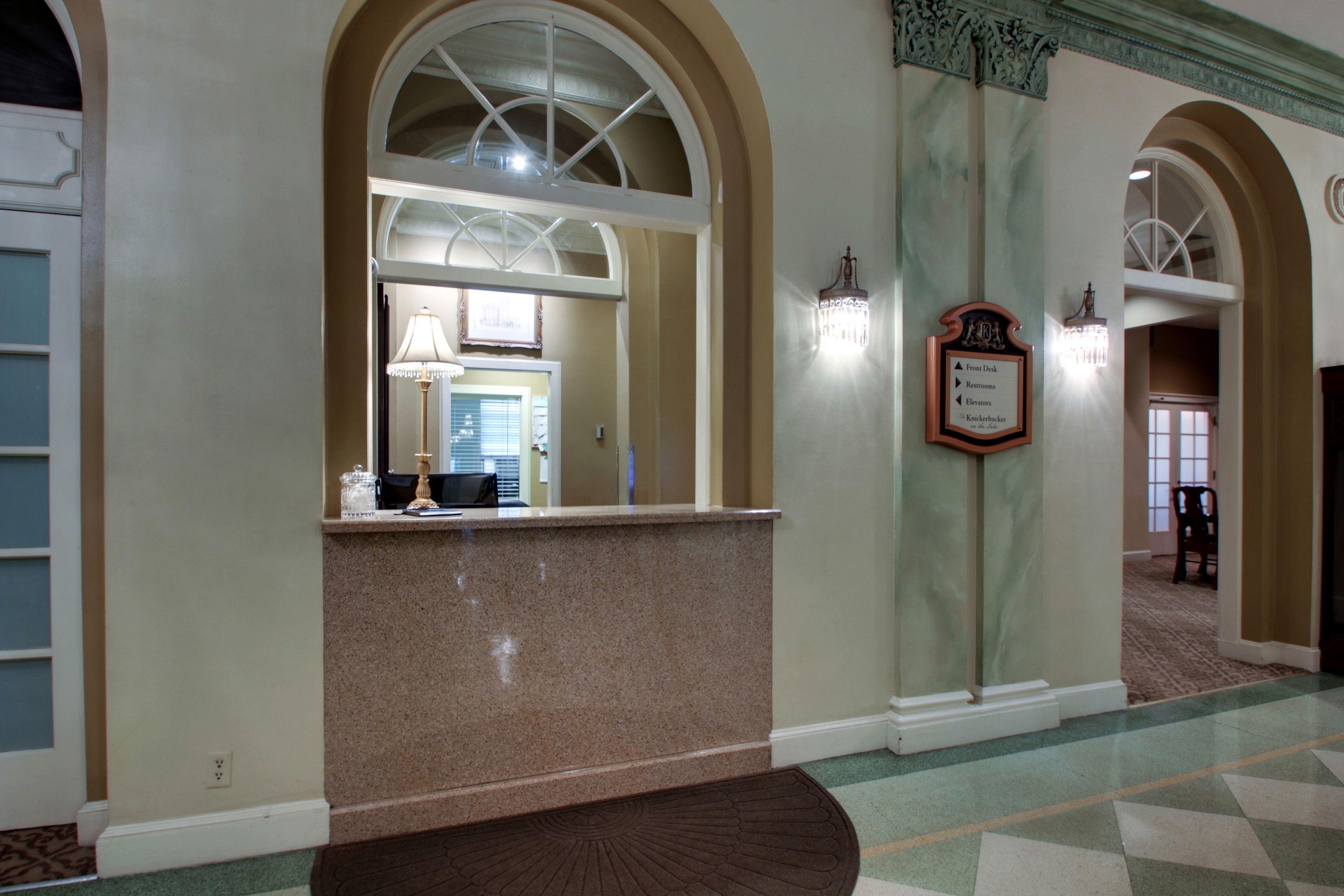 A reception area with a marble counter, a chandelier, and a wall-mounted sign indicating the direction to the front desk, elevators, and restrooms.