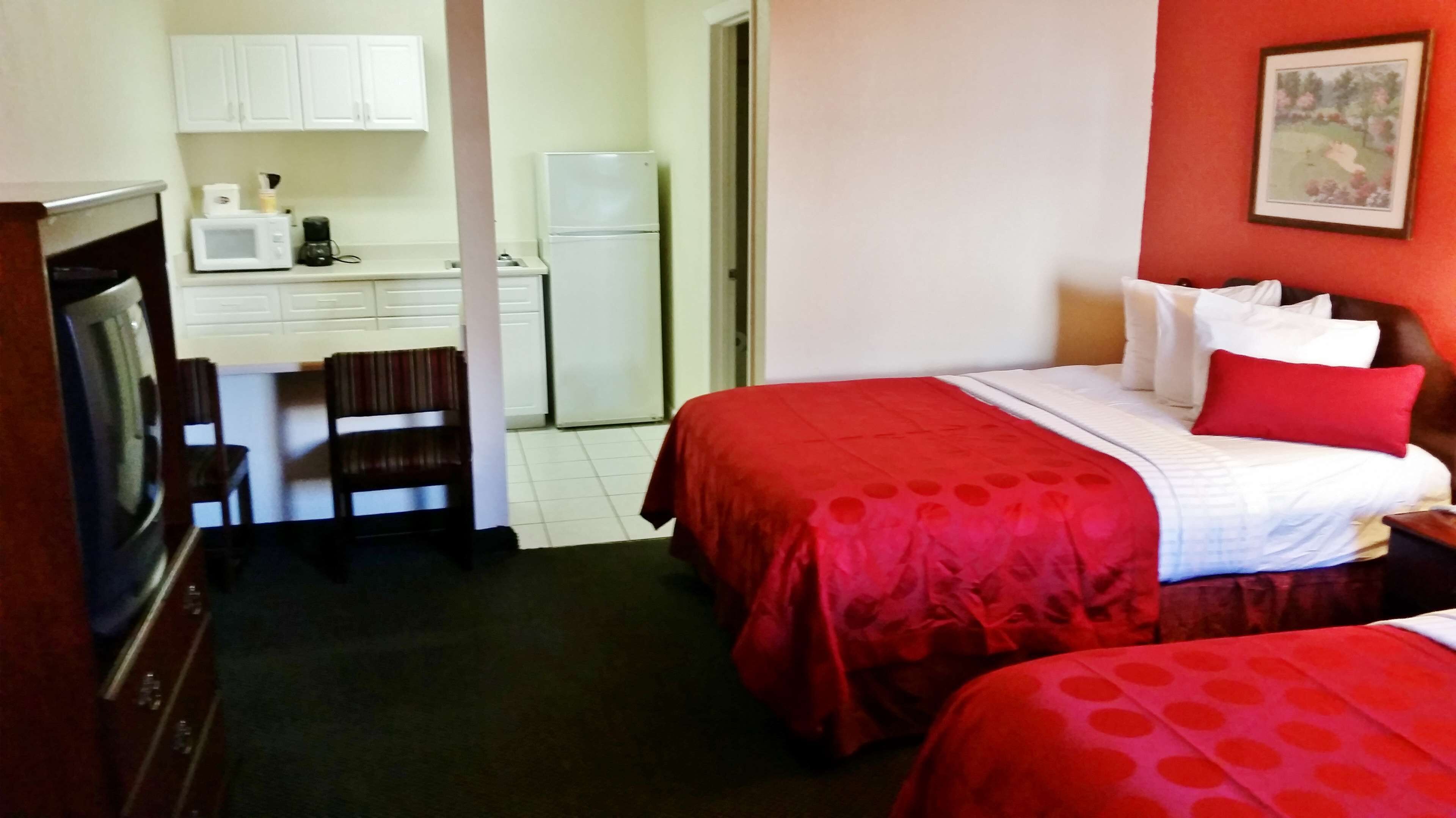 Une chambre d’hôtel avec deux lits, une kitchenette, une télévision et une porte donnant sur une salle de bain.