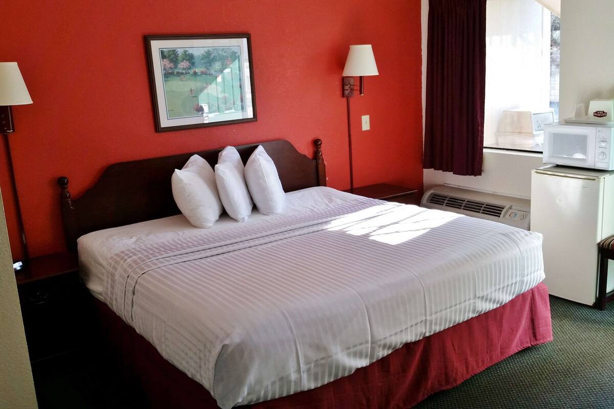 A hotel room with a bed, two bedside lamps, a framed picture on the wall, a microwave, and a small table with a tissue box.