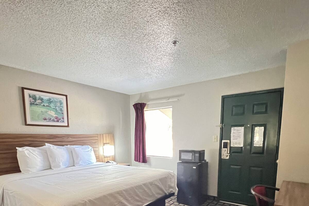 A hotel room with a bed, a television, a desk, and a green door.