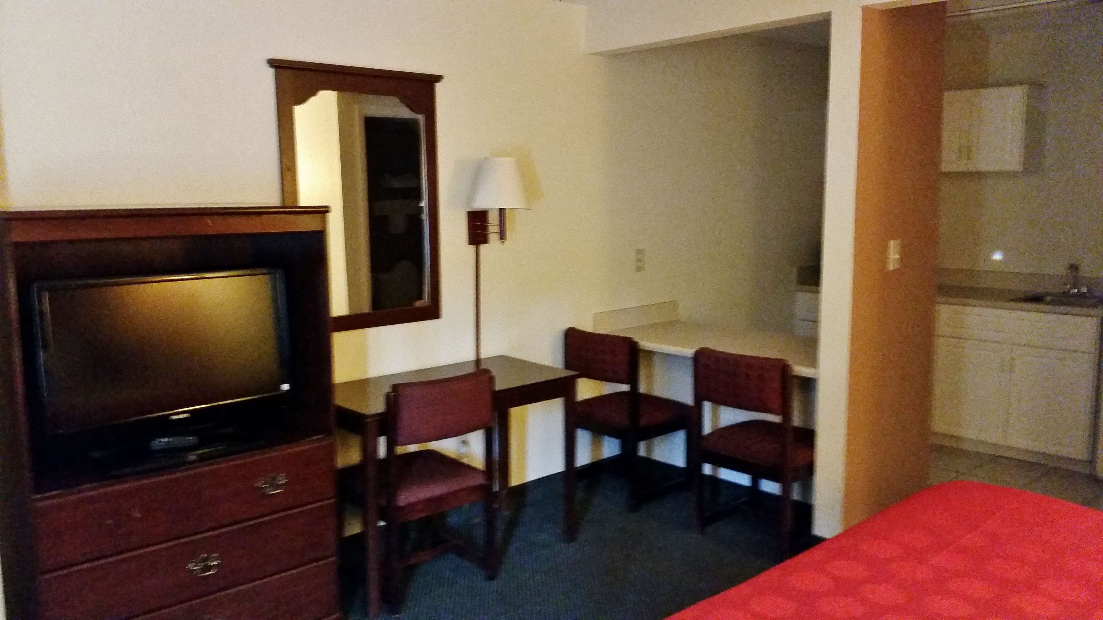 Ein Hotelzimmer mit Fernseher, Schreibtisch mit Stühlen, Spiegel und Küchenzeile.